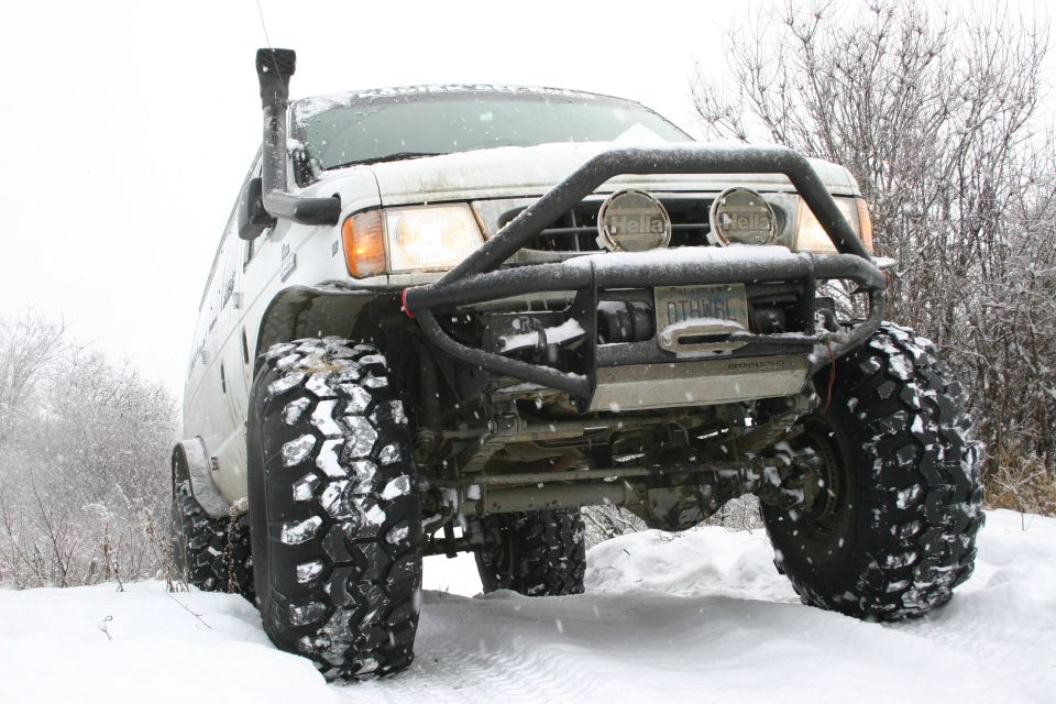 White van with snorkel and big tires in snow. Has Hella lights on a bull bar