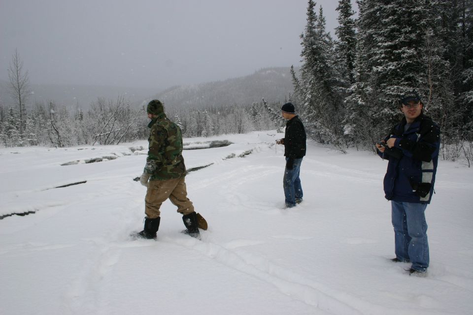 Three men stand in a snow-covered landscape with trees in the background