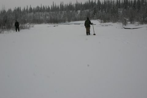 2003 Jeep TJ - Two individuals are in a wide, snow-covered area with a forest in the distance.