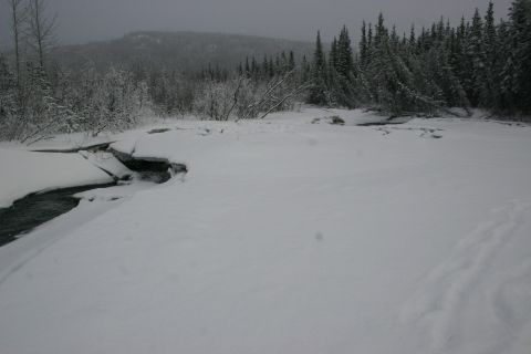 2003 Jeep TJ - A winter scene shows a partially frozen stream winding through snow-covered ground, with trees lining the horizon.