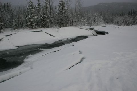 2003 Jeep TJ - A frozen river winds through a snow-covered landscape with trees lining the banks.