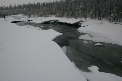 2003 Jeep TJ - A lone figure stands by a partially frozen river in a snowy, wooded landscape.