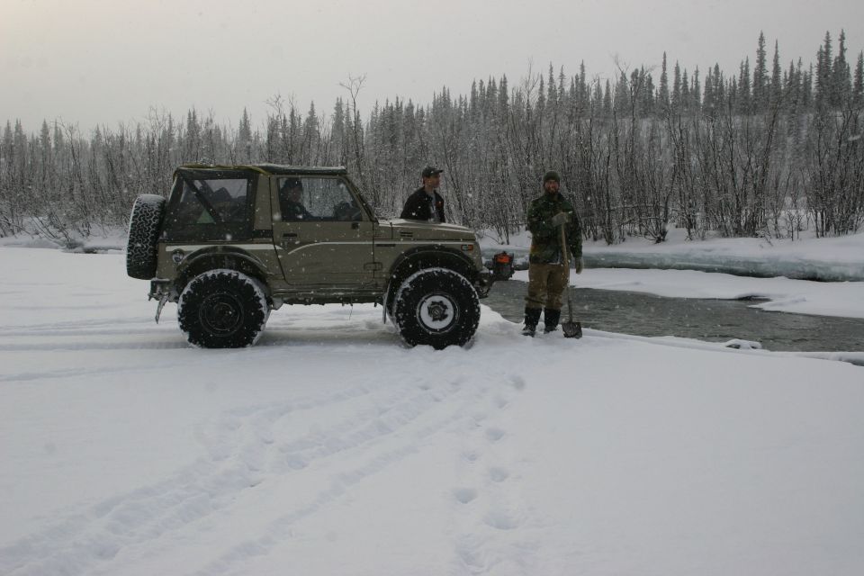 Off-road vehicle with two people standing next to it in a snowy landscape near a partially frozen river
