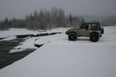 2003 Jeep TJ - A Suzuki Samurai navigates a snowy landscape beside a cold river.