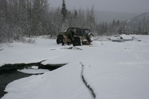 2003 Jeep TJ - A green Jeep TJ navigates a snowy, icy trail with a person tending to the vehicle.