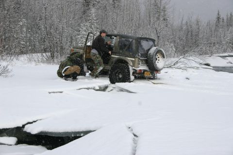 2003 Jeep TJ - A 2003 Jeep TJ navigates snowy terrain near a partially frozen body of water.