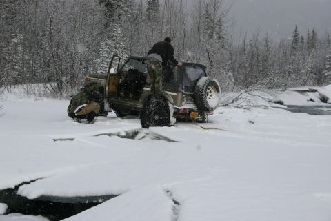2003 Jeep TJ - An off-road vehicle is stuck in the snow with people attempting to free it.