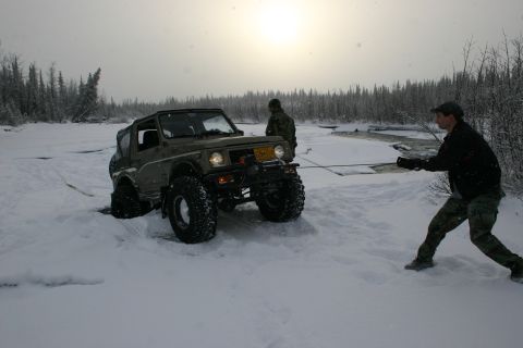 2003 Jeep TJ - A man pulls a stuck Suzuki Samurai with a rope in a snowy, wooded area.