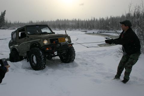 2003 Jeep TJ - A man pulls a Suzuki Samurai with a winch cable through a snowy landscape.