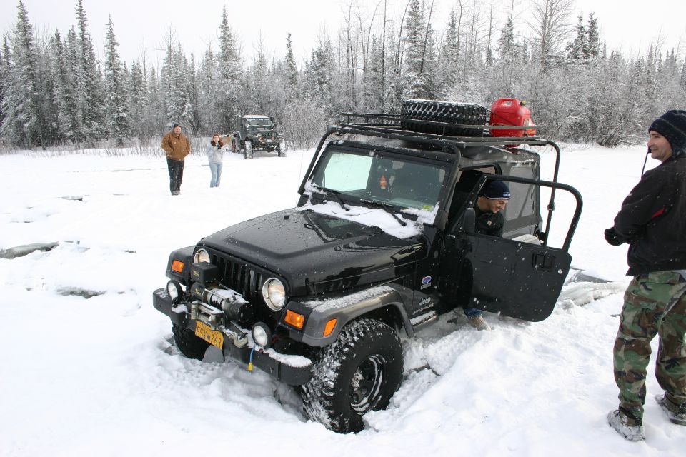Black Jeep Wrangler stuck in snow, front winch, roof rack with spare tire and red gas can, driver's door open