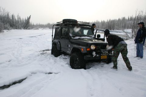 2003 Jeep TJ - A black Jeep Wrangler is stuck in a snowy landscape with three people nearby, one appearing to be winching it.