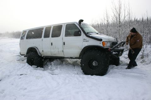 2003 Jeep TJ - A man attempts to free a white van that is stuck in deep snow, equipped with oversized tires and a snorkel.