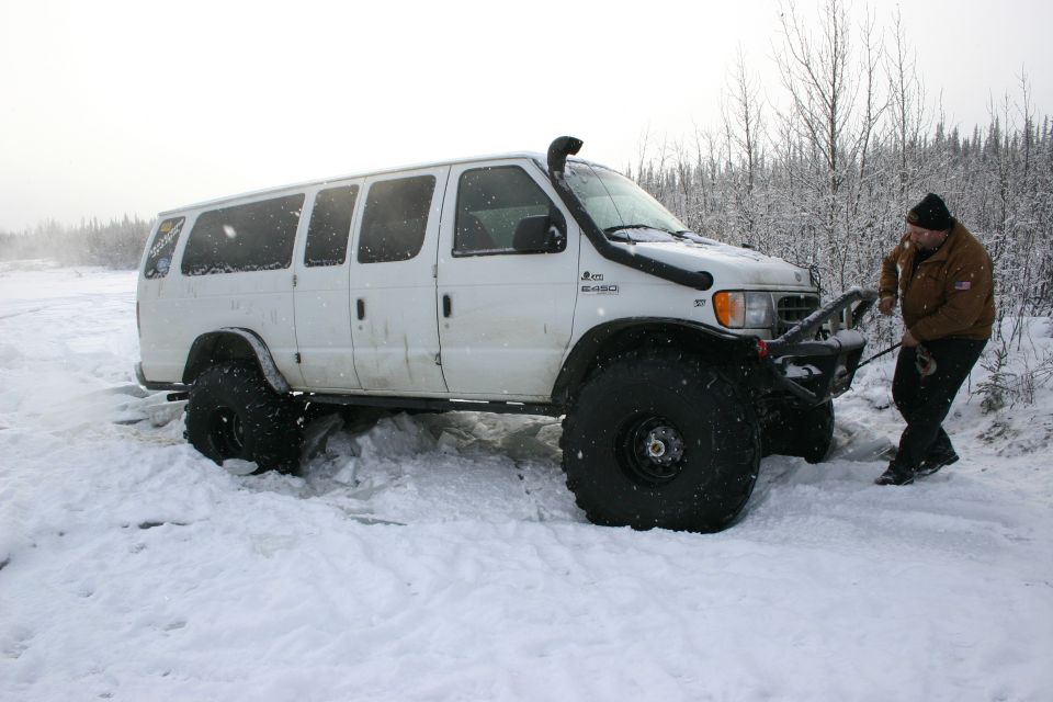White van with large tires and snorkel stuck in snow, man pulling on a winch cable