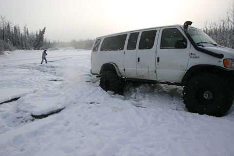 2003 Jeep TJ - A white van with large off-road tires is stuck in the snow, with a person standing in the distance.