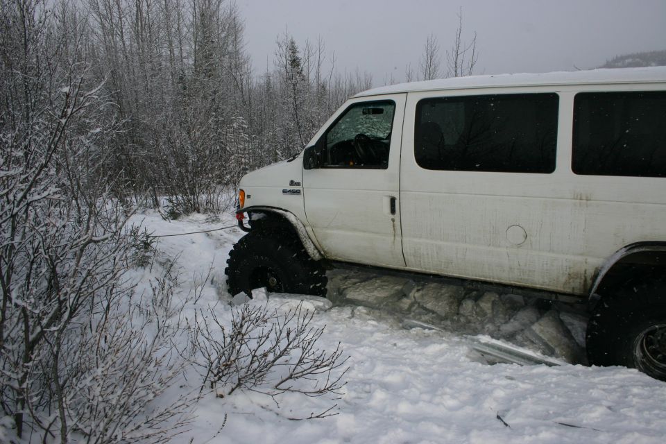 White van with large tires stuck in snow, with a tow rope attached