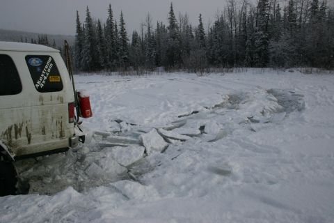 2003 Jeep TJ - A white SUV is stuck in a patch of broken ice on a snowy trail, with a forest in the background.