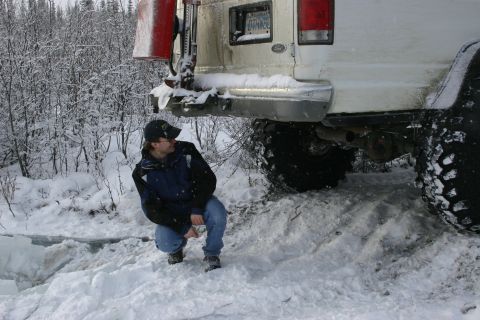 2003 Jeep TJ - A person crouches near the rear of a white SUV partially submerged in snow, suggesting it may be stuck.