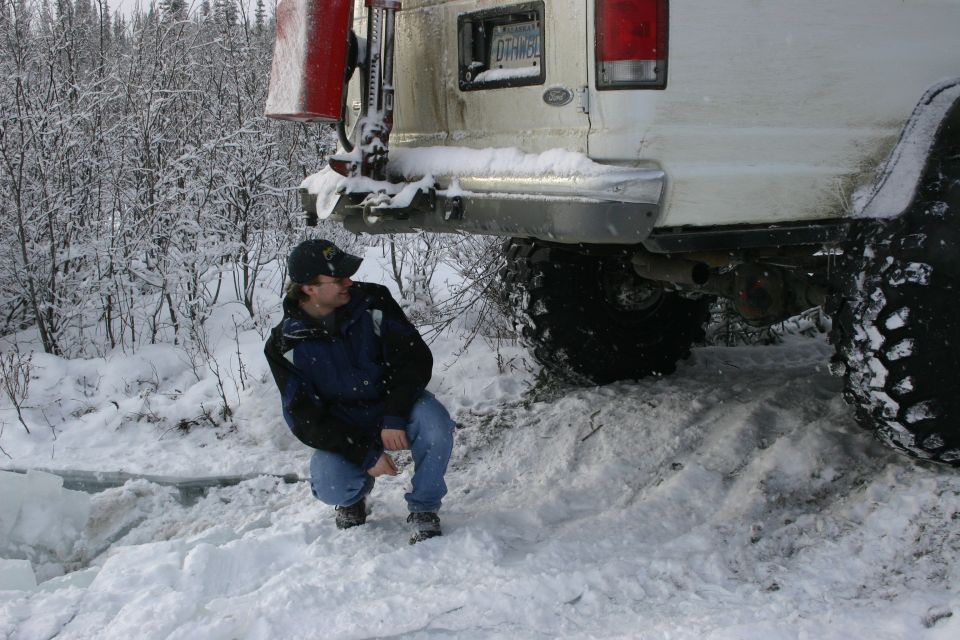 Rear view of a white SUV stuck in snow, with a person crouching nearby