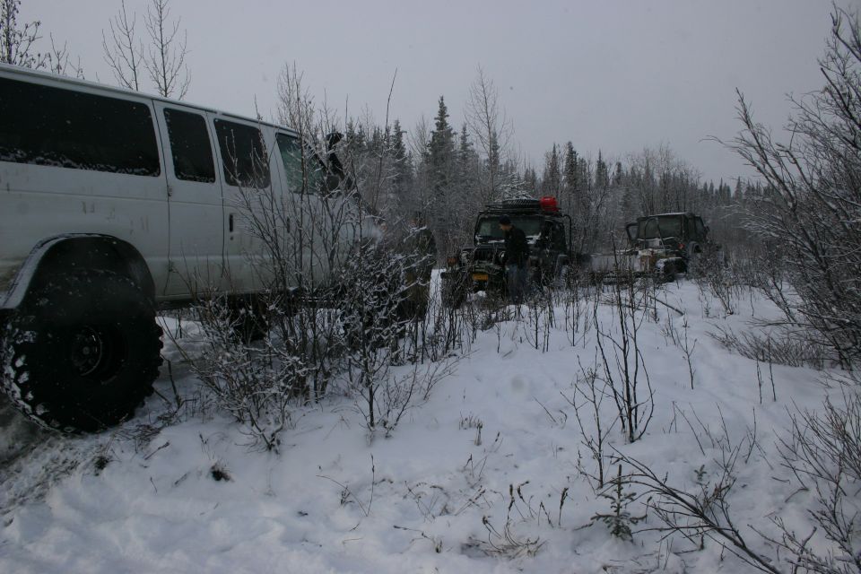 White van with large tires and two off-road vehicles in snowy woods