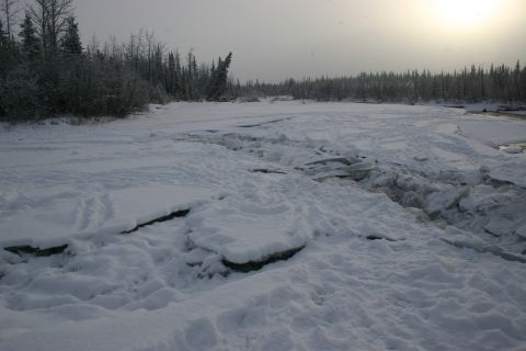 2003 Jeep TJ - A frozen riverbed with ice chunks and snow covers the ground, bordered by trees.