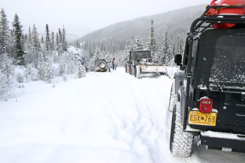 2003 Jeep TJ - Multiple off-road vehicles, including Jeeps and a snowplow, navigate a snowy trail in a wooded mountain area.