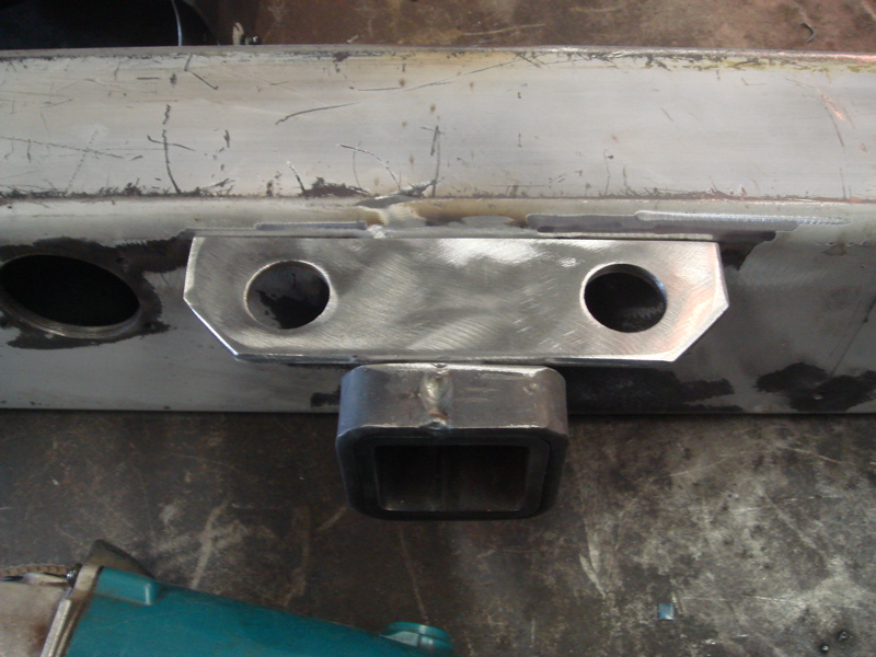 Close-up of a custom trailer hitch receiver welded onto a metal frame, with two bolt holes visible