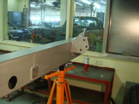1996 Ford Bronco - A metal bumper part is mounted on an orange stand in a workshop. A Chevrolet truck is visible through the window in the background.