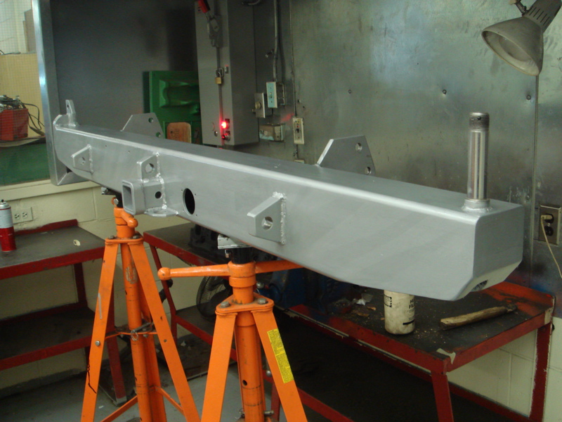 Silver metal rear bumper assembly mounted on orange jack stands in a workshop