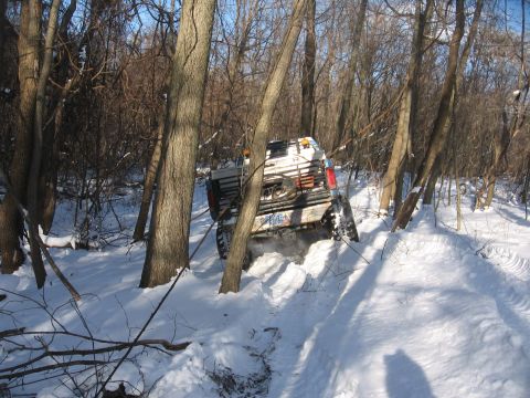 1979 Ford Bronco - A vehicle navigates a snowy trail, its tires digging into the deep snow as it maneuvers through a wooded area.