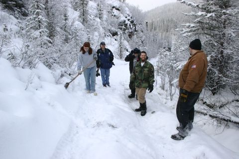 2003 Jeep TJ - A group of people are gathered on a snow-covered trail in a mountainous area, with one person actively shoveling snow.