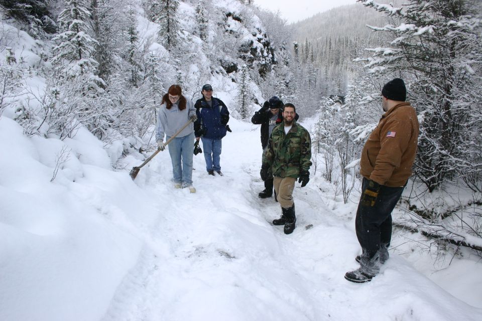 Group of people in a snowy mountain landscape, one shoveling snow