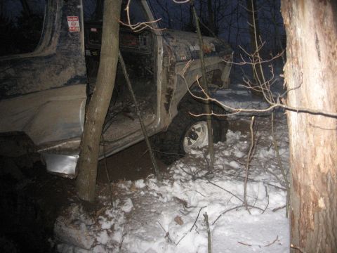 1979 Ford Bronco - A vehicle is stuck in a wooded area with snow and mud on the ground.