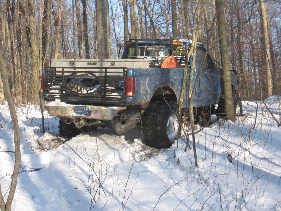blue pickup truck with large tires stuck in snow, rear view. License plate reads 2890 GG