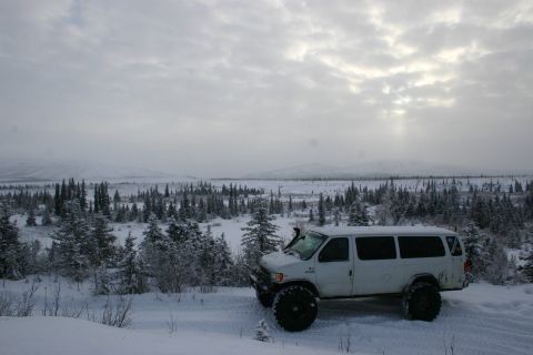 2003 Jeep TJ - A white van equipped with large off-road tires and a snorkel sits in a snowy landscape under a cloudy sky.