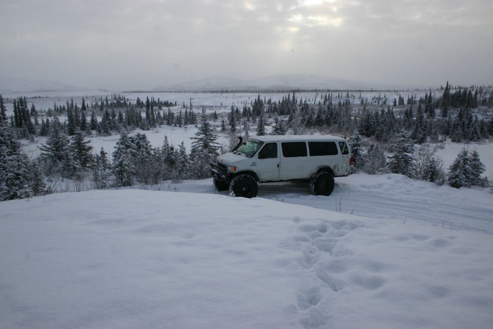 White van with snorkel and oversized tires parked on a snowy hill overlooking a forest