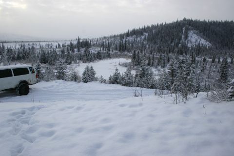 2003 Jeep TJ - A white van is parked on a snow-covered road, surrounded by a winter landscape of pine trees and hills.