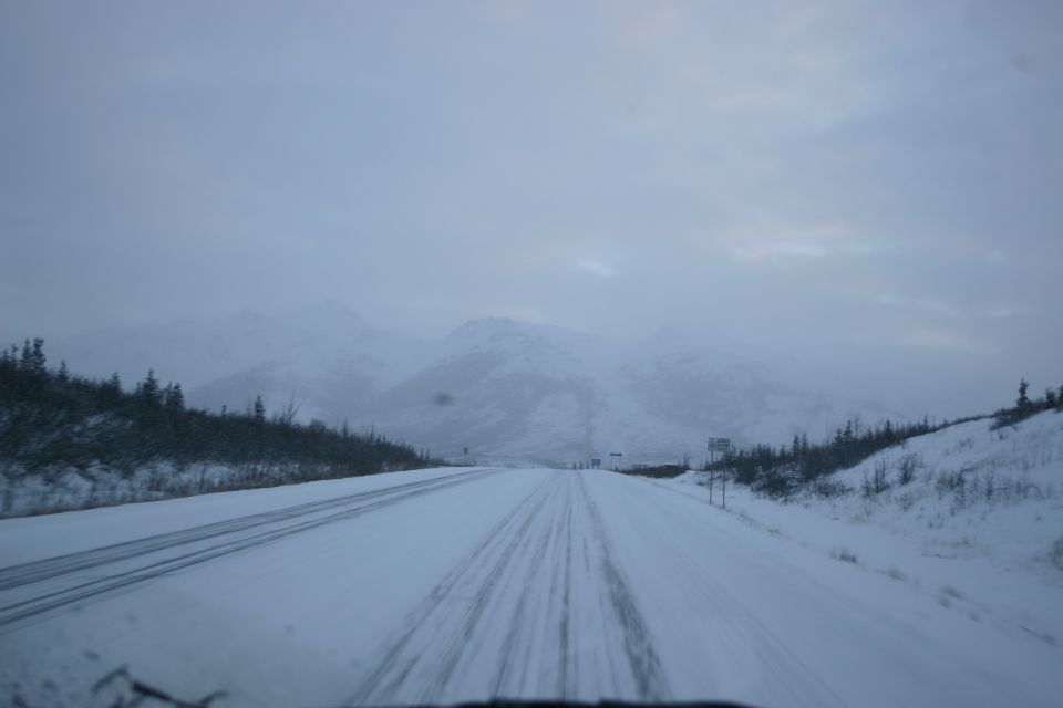Snowy road with tire tracks leading towards mountains under a cloudy sky