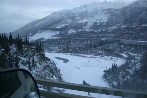 2003 Jeep TJ - A winter scene shows a frozen river valley surrounded by snow-covered mountains and evergreen trees.