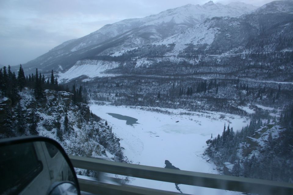 view from car window of snow-covered mountains and a frozen river valley