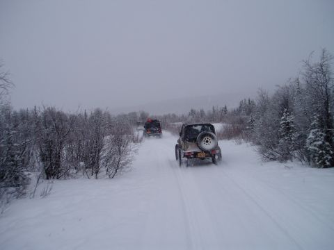 2000 Ford E350 - Multiple off-road vehicles travel down a snow-covered path surrounded by trees.