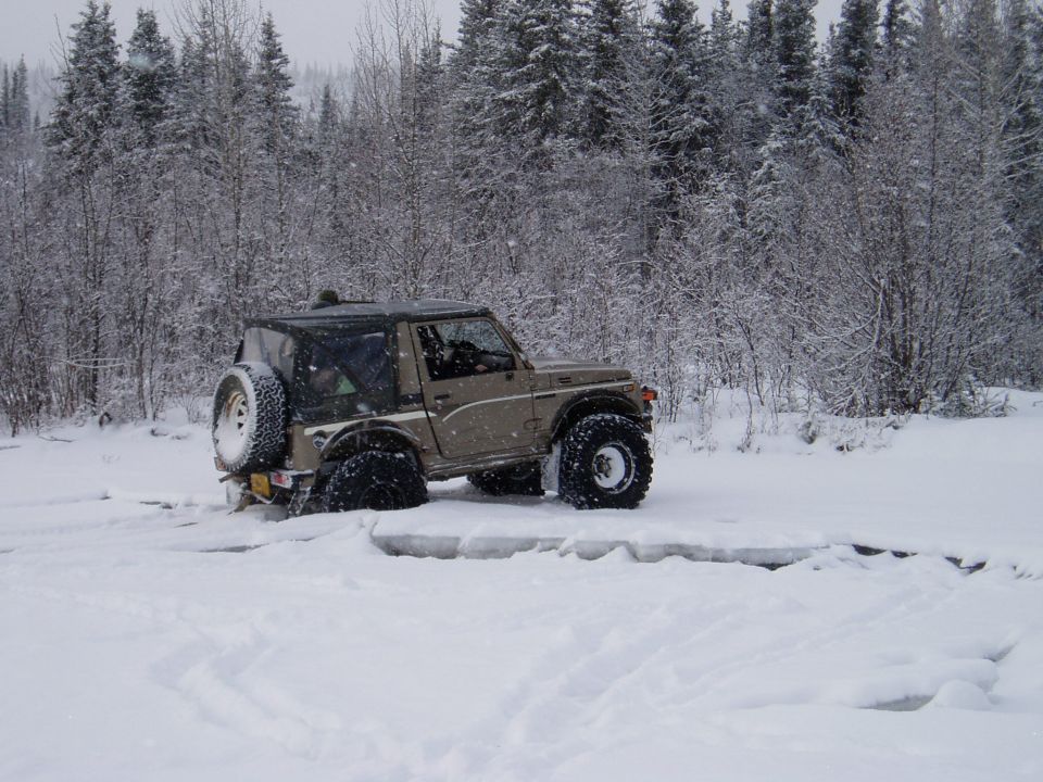 Off-road vehicle with large tires stuck in deep snow, trees in background