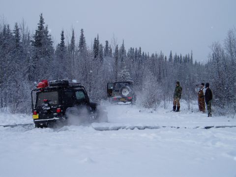 2000 Ford E350 - Two off-road vehicles navigate a snowy path surrounded by trees, with people observing.