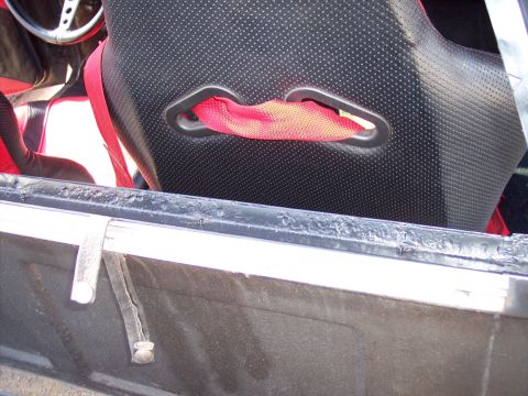 1972 Ford Ranchero - The interior of a vehicle shows a black racing seat with red accents and a red safety harness.