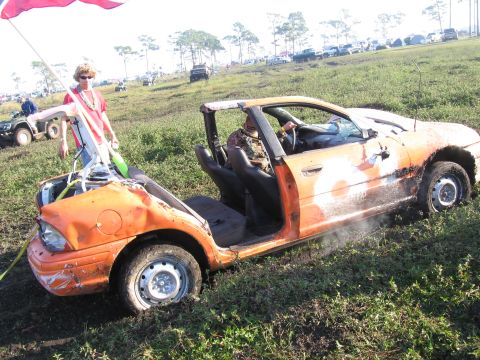 1974 Ford F-100 - Orange-painted beater sedan converted into a mud-field play car, roof and doors cut away and body dented, sitting on plain steel wheels in…
