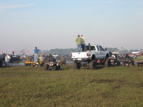1974 Ford F-100 - Two men stand in the bed of a white lifted Ford Super Duty crew-cab pickup on tall mud tires and a snorkel-style stack, using it as a viewi…