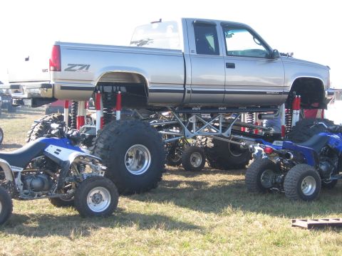1974 Ford F-100 - Passenger-side view of a silver two-tone GMC Sierra 1500 Z71 extended-cab pickup on an extreme long-travel lift with a tubular four-link/tr…