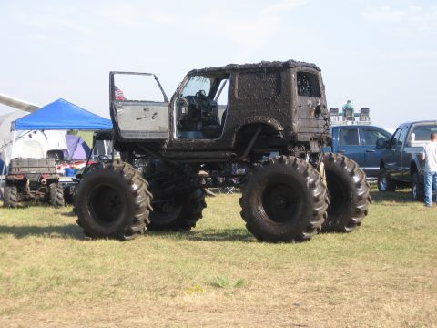 1974 Ford F-100 - Mud-caked lifted Jeep CJ mud truck photographed from the side in a grassy event field, doors open and body plastered with thick brown mud.…