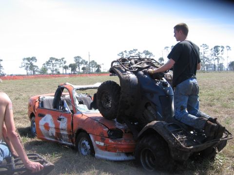 1974 Ford F-100 - A quad bike is positioned on top of a wrecked orange convertible car in a grassy field.