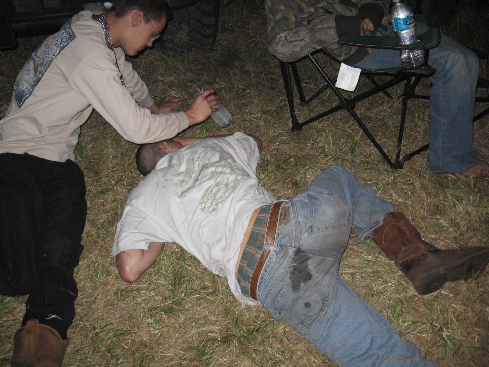 guy giving water to another guy lying on the ground, another person sits in a chair nearby