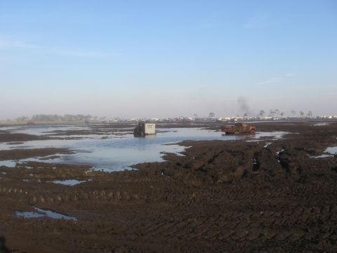 1974 Ford F-100 - Wide daylight view across a churned mud-bog field, deep tire ruts and standing water in the foreground under a clear blue sky. A white box-…
